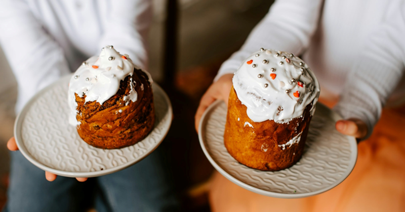 Two young children hold out plates with iced cakes on them