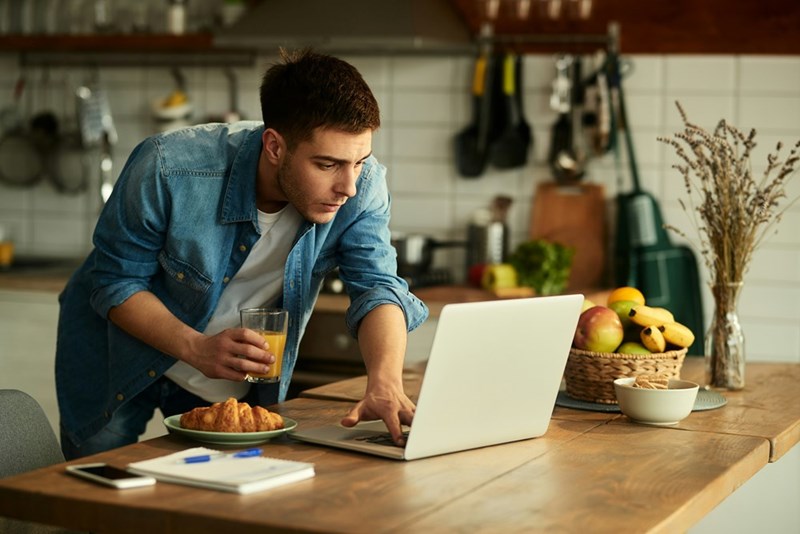 A remote employee stands from his desk to refill his drink while eating lunch during a Zoom meeting.