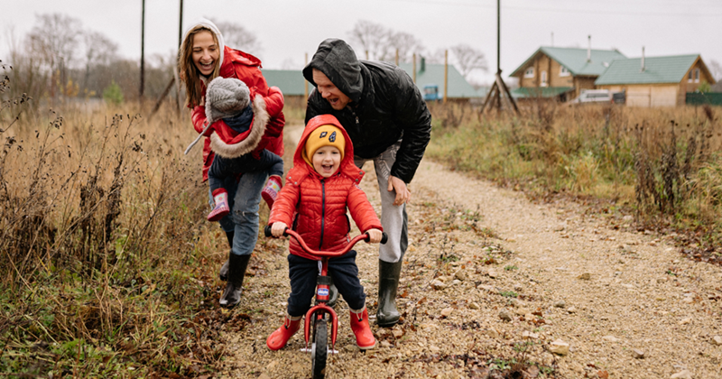 Family playing together outside with young children on a bike. 