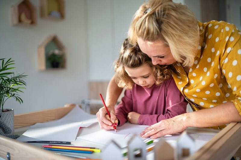 A cute small girl with mother in bedroom indoors at home drawing pictures