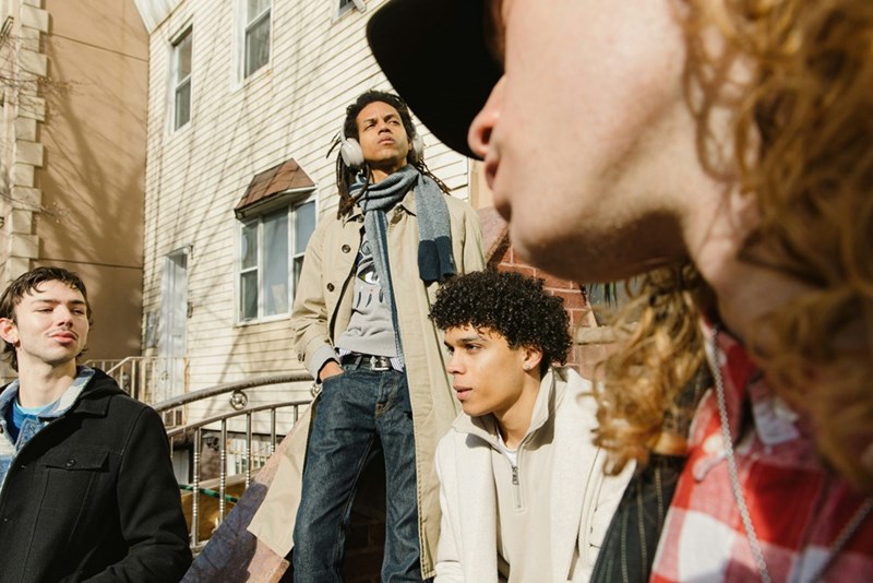 Neighbors talking outside their apartment building, but one of them seems distant, reflecting conflict or tension.