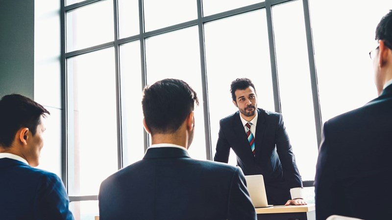 The employee's manager speaks to the team in a conference room.