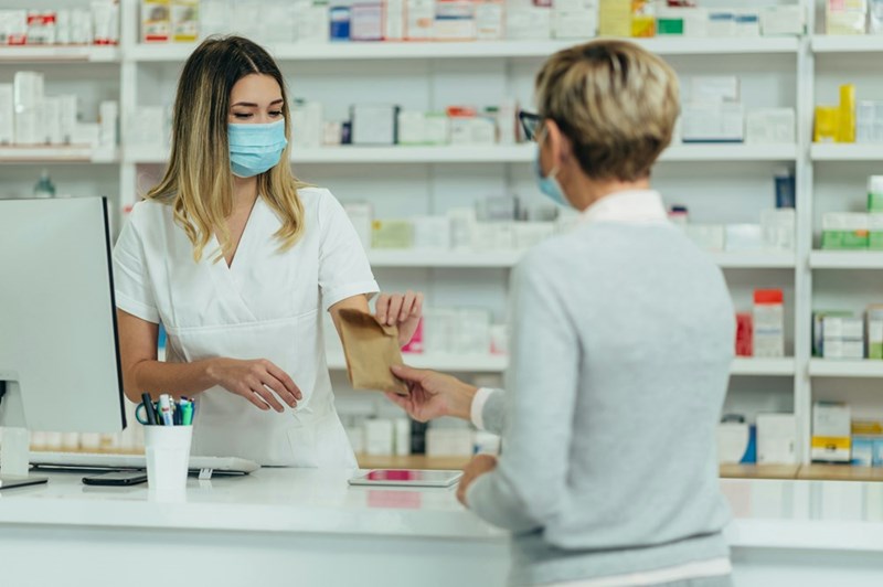 Female pharmacist wearing protective mask and give a customer in a pharmacy a paper bag full of medications