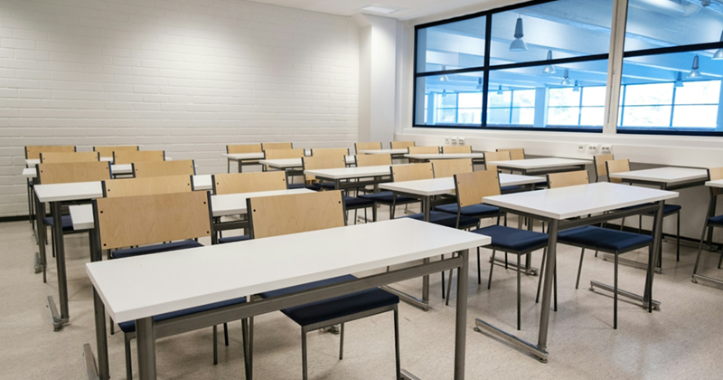 An empty classroom filled with desks and chairs next to a large window