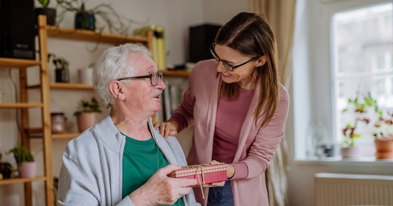 A woman visits her senior father in his home and hands him a present.