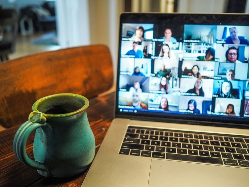 A coffee mug on a desk next to a Zoom call with dozens of attendees present.