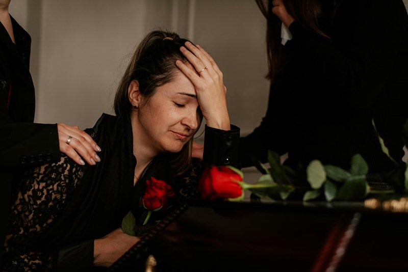 A woman sitting at a coffin with her hands on her head