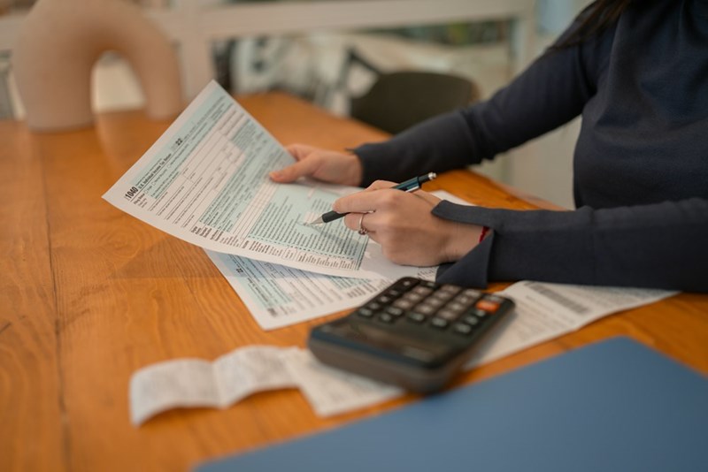 A woman calculating rent and utility costs with a calculator and receipts, representing the challenges of dividing expenses between rommates