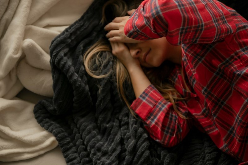 A woman lays on top of a blanket, trying to go to sleep
