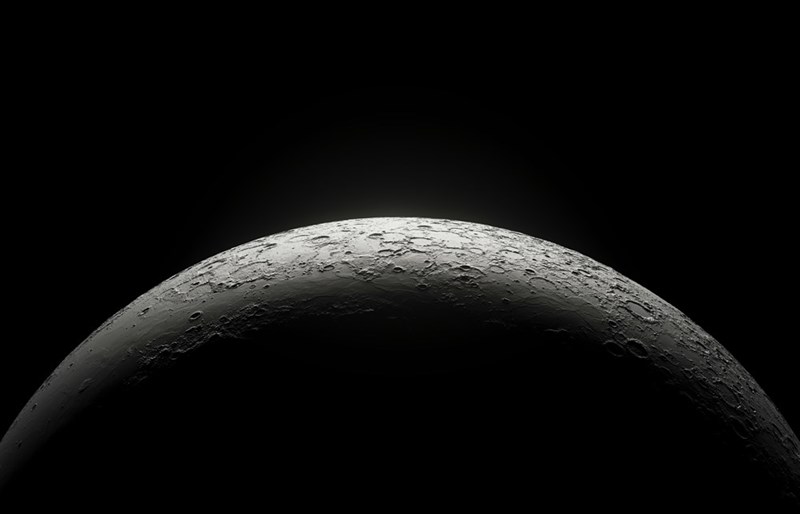 The Moon’s rugged surface emerges from darkness, lit softly along its curved edge.