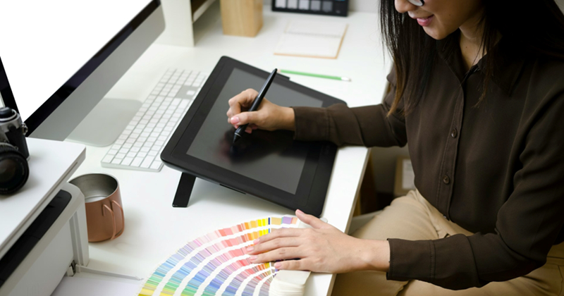 A woman in business attire who is drawing on a tablet consults a color chart