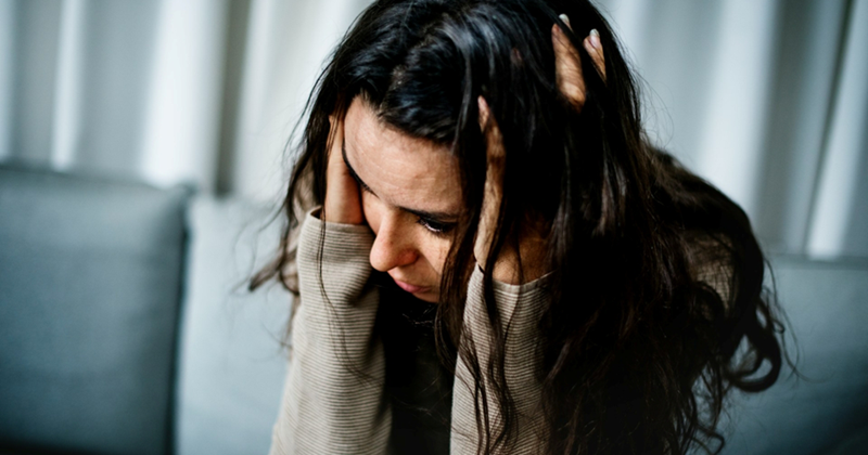 An upset woman clutches her head with both hands while sitting on a couch