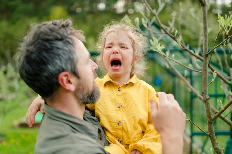 A father holding his crying little daughter and comforting her in a garden