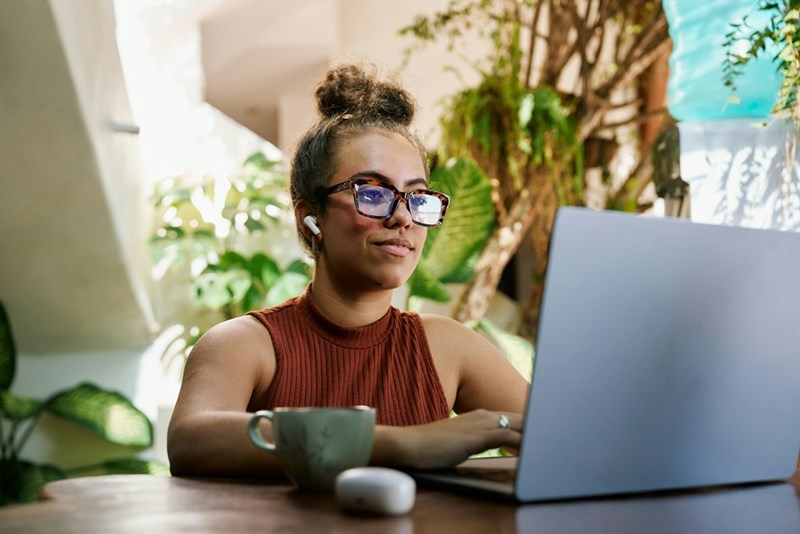 A woman sits in front of a laptop computer in a room with plants
