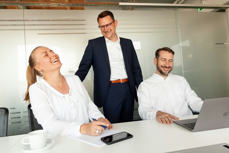 Three colleagues laughing together in an office setting