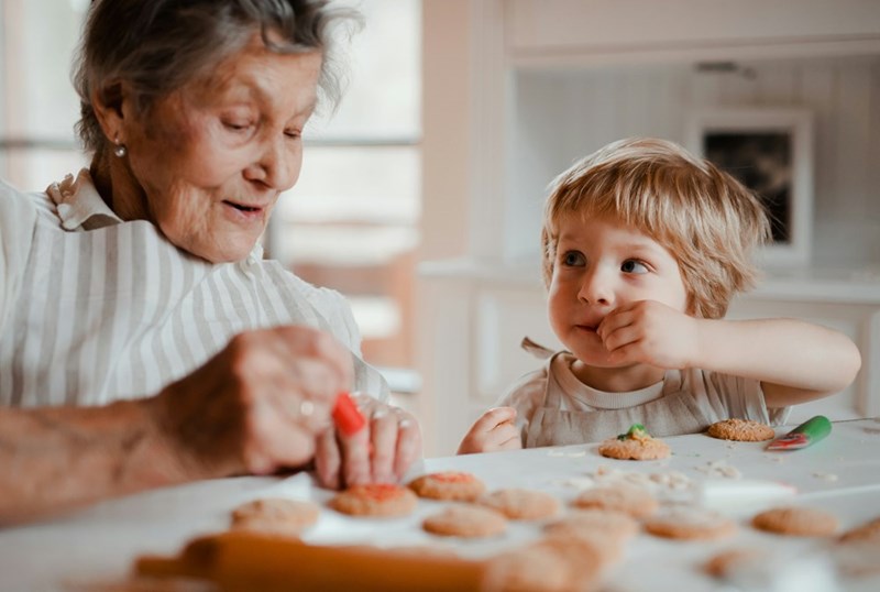 Toddler looks up adoringly at grandmother while they decorate cookies together.