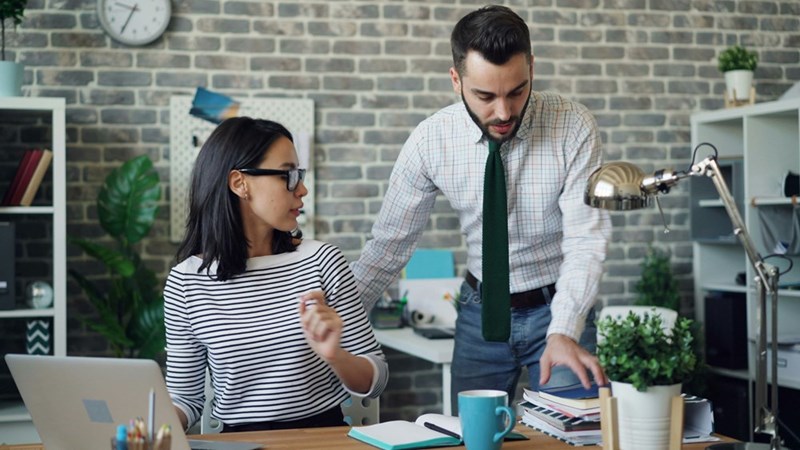 A boss talks to his female employee at her desk