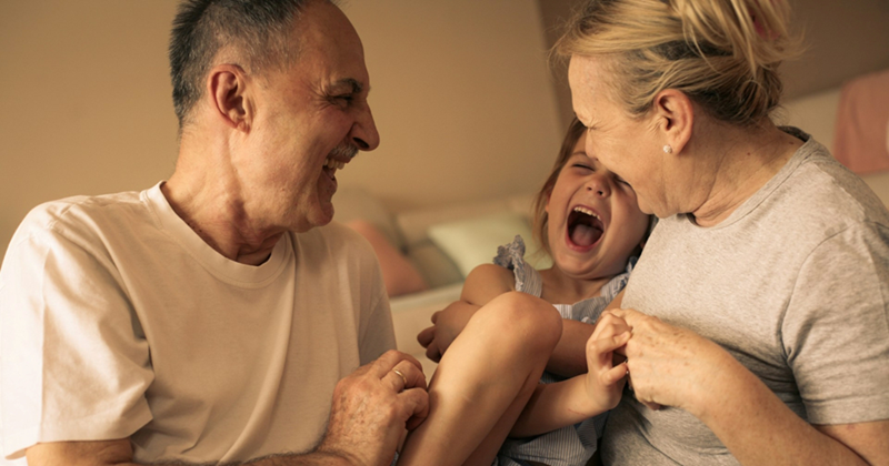 A little girl laughs while sat between her grandparents inside at night