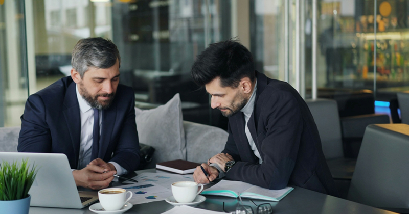 Two businessmen look at the documents on the table in front of them where they are sitting