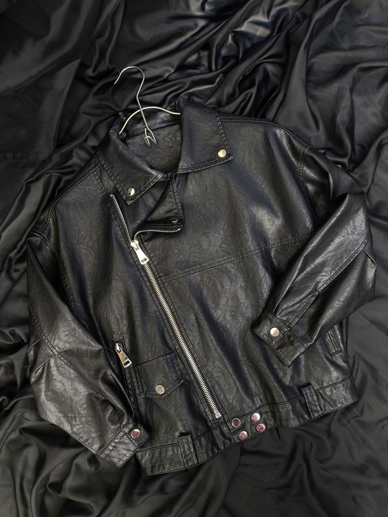 A black leather jacket laying on top of a bed