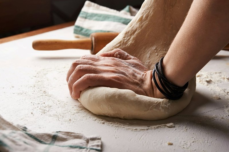 A loaf of sourdough is roughly kneaded on a bench top