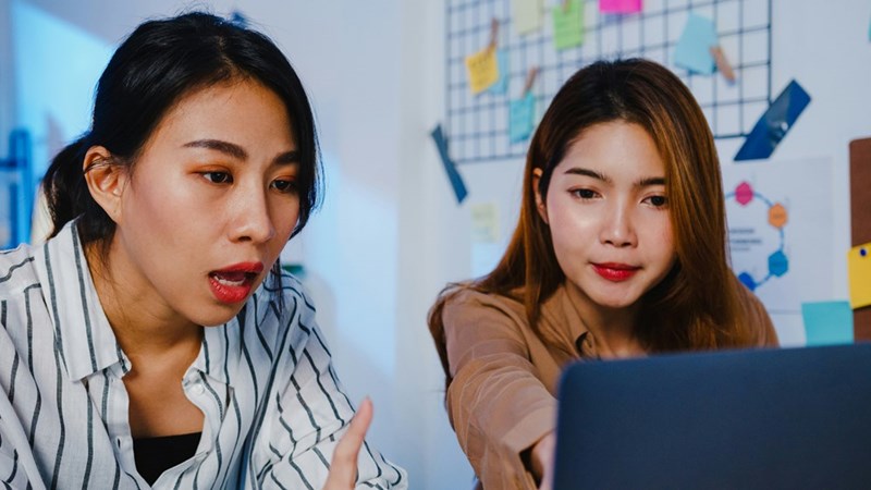 Two women look surprised and focused while reacting to something on a laptop.