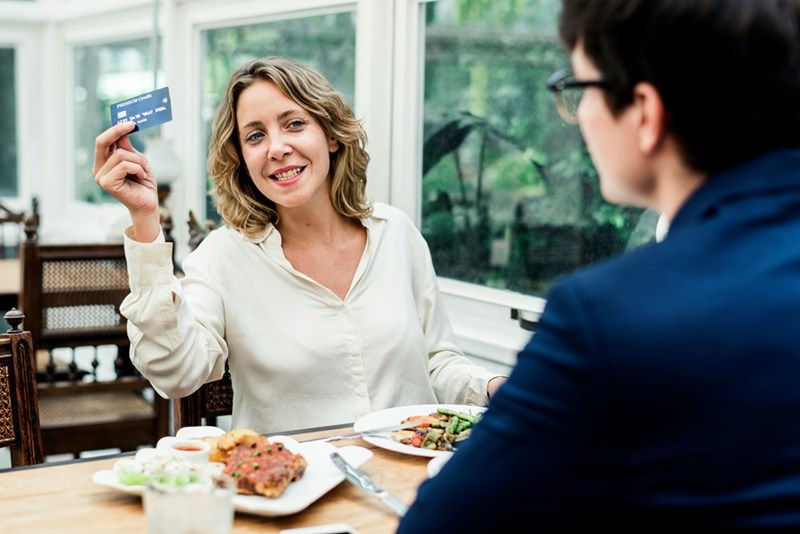 Woman holding credit card while dining at a restaurant with a man