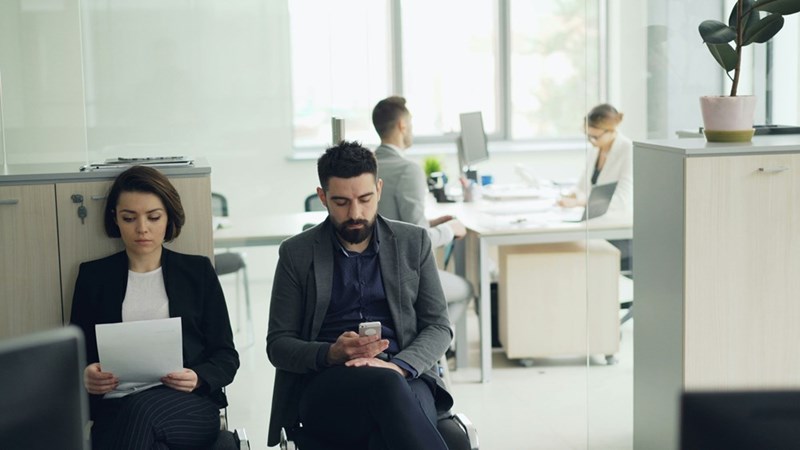 Two people waiting in an office library for a job interview
