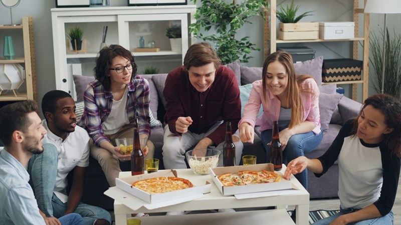 Friends eating pizza at a house gathering, with both hypoallergenic and regular pizza options on the table.