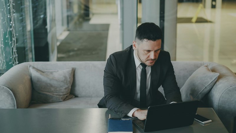 A man in a suit working on laptop while sitting on an office sofa.