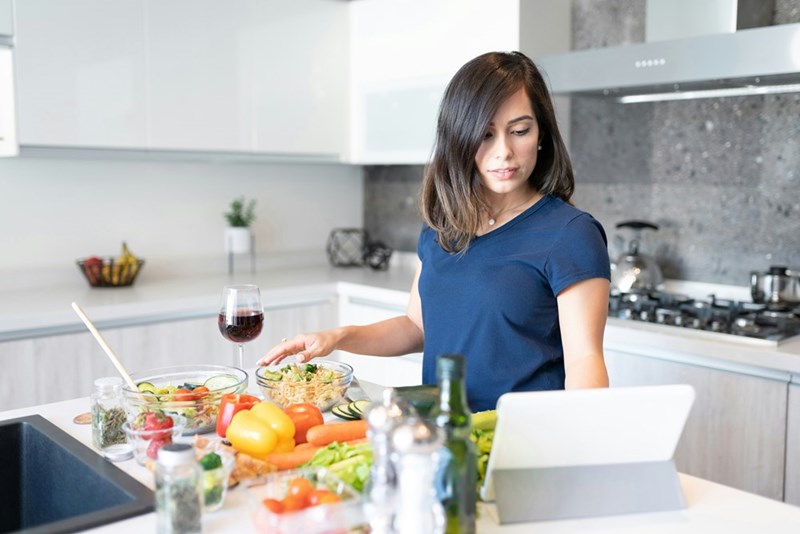 A woman cooking a special meal for her friend, carefully following a recipe on her tablet.