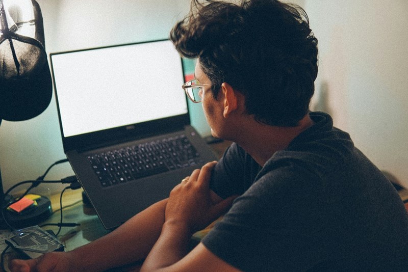 A man sits in front of his laptop at work, contemplating