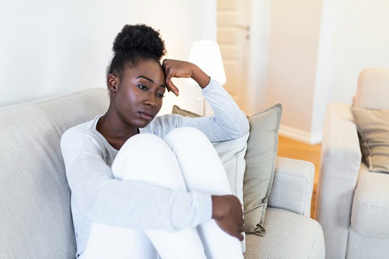 Sad, thoughtful, worried African American girl sits on sofa looking away
