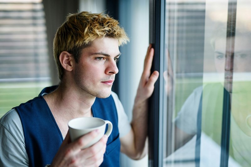 A young man looking out his apartment's window, keeping an eye on the surroundings.