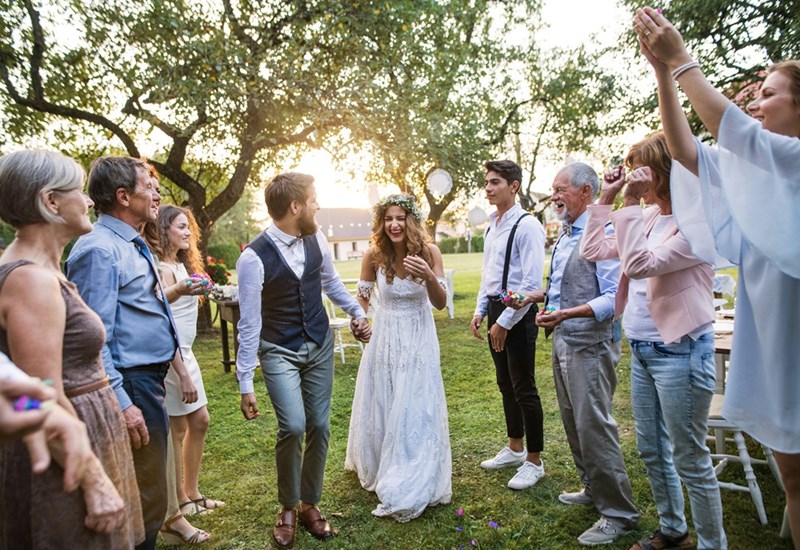 A outdoor wedding moment as the couple walks hand in hand through cheering guests in a sunlit garden.
