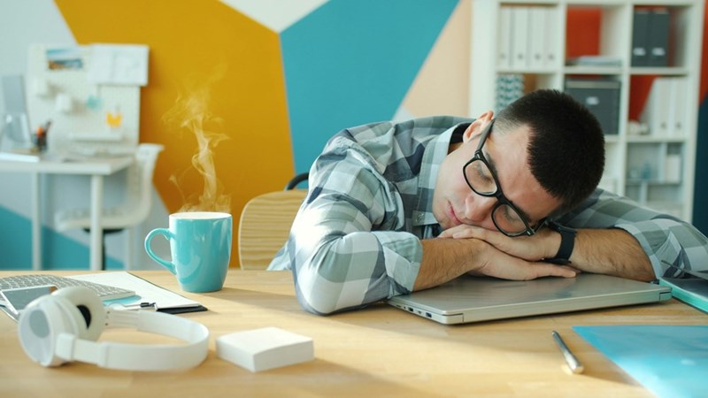 A man sleeping at his desk with a coffee and laptop