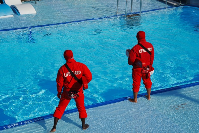 Two men in red lifeguard suits standing in front of a swimming pool