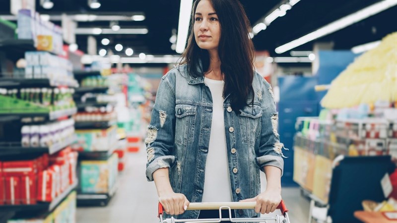 Woman looks concerned at lack of food price labels as she shops.