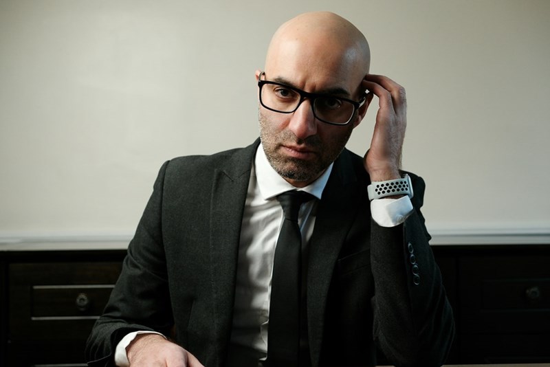 A bald man in a suit and tie sitting at a table and contemplating