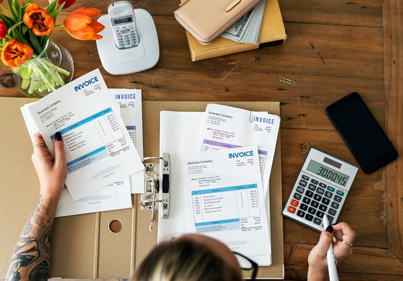 A woman does accounting on a table with documents strewn about