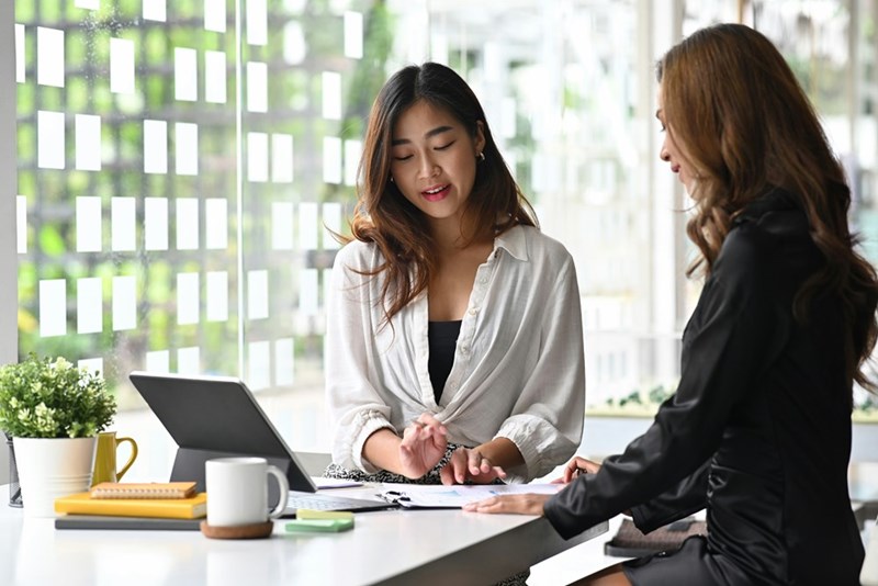 A young employee in her twenties assists another coworker, who is a few years younger, in the office.