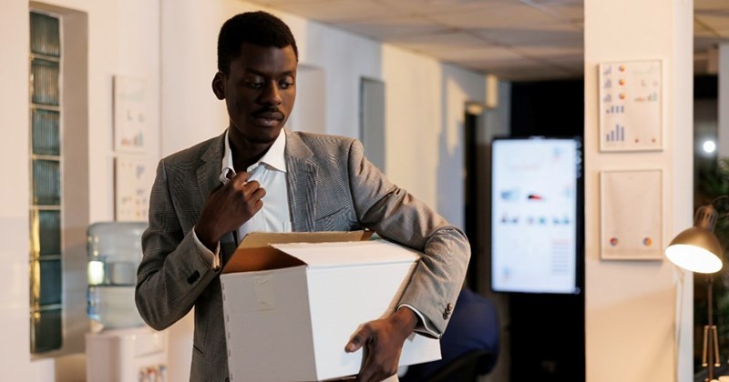 An employee carries a box of belongings in an empty office.