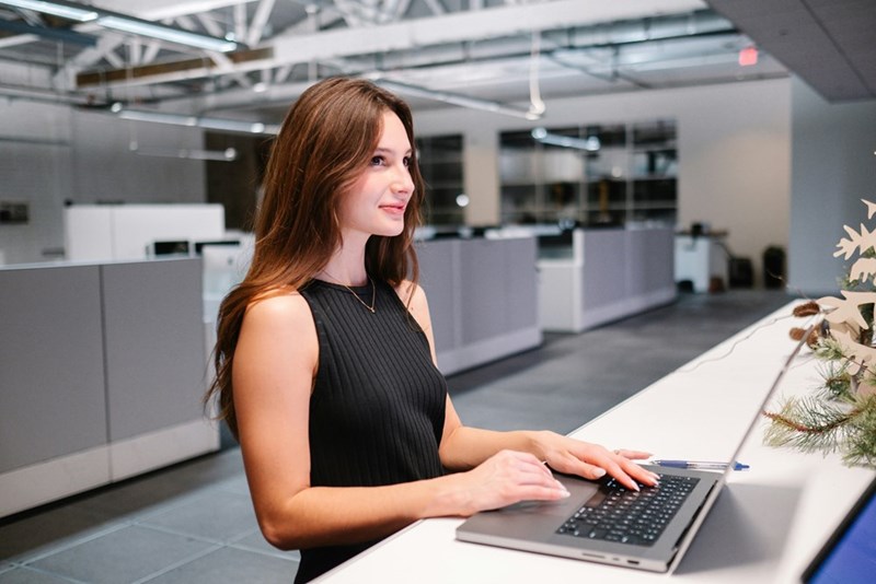 A woman in a black dress works at her laptop at the office