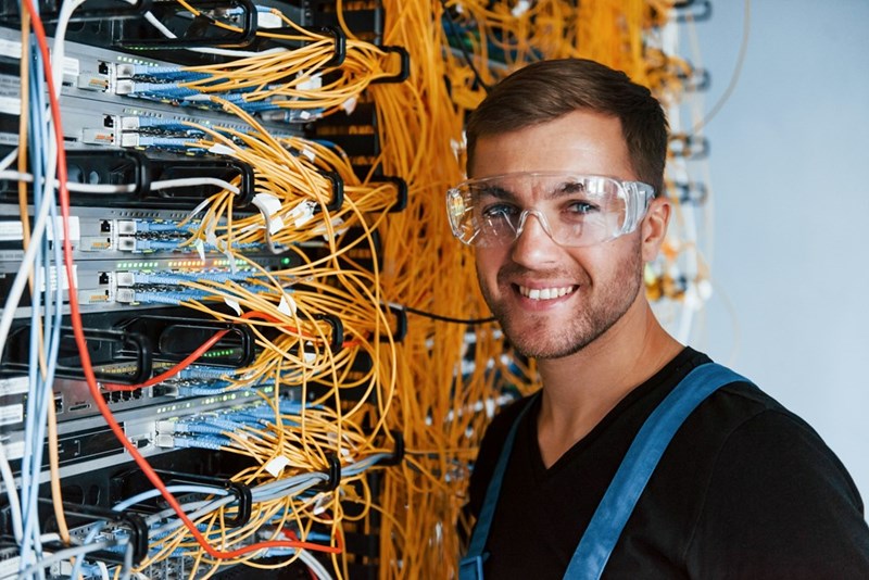 IT employee working in tech, wearing safety glasses, smiling as he works