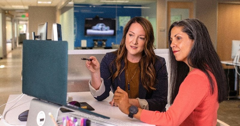 Two female coworkers helping one another in the office.