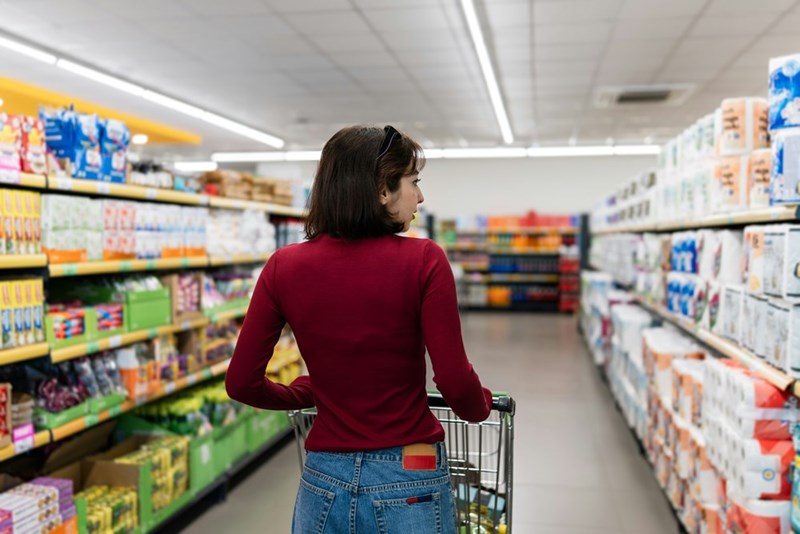 Woman examining supermarket shelves while walking through the aisle. 
