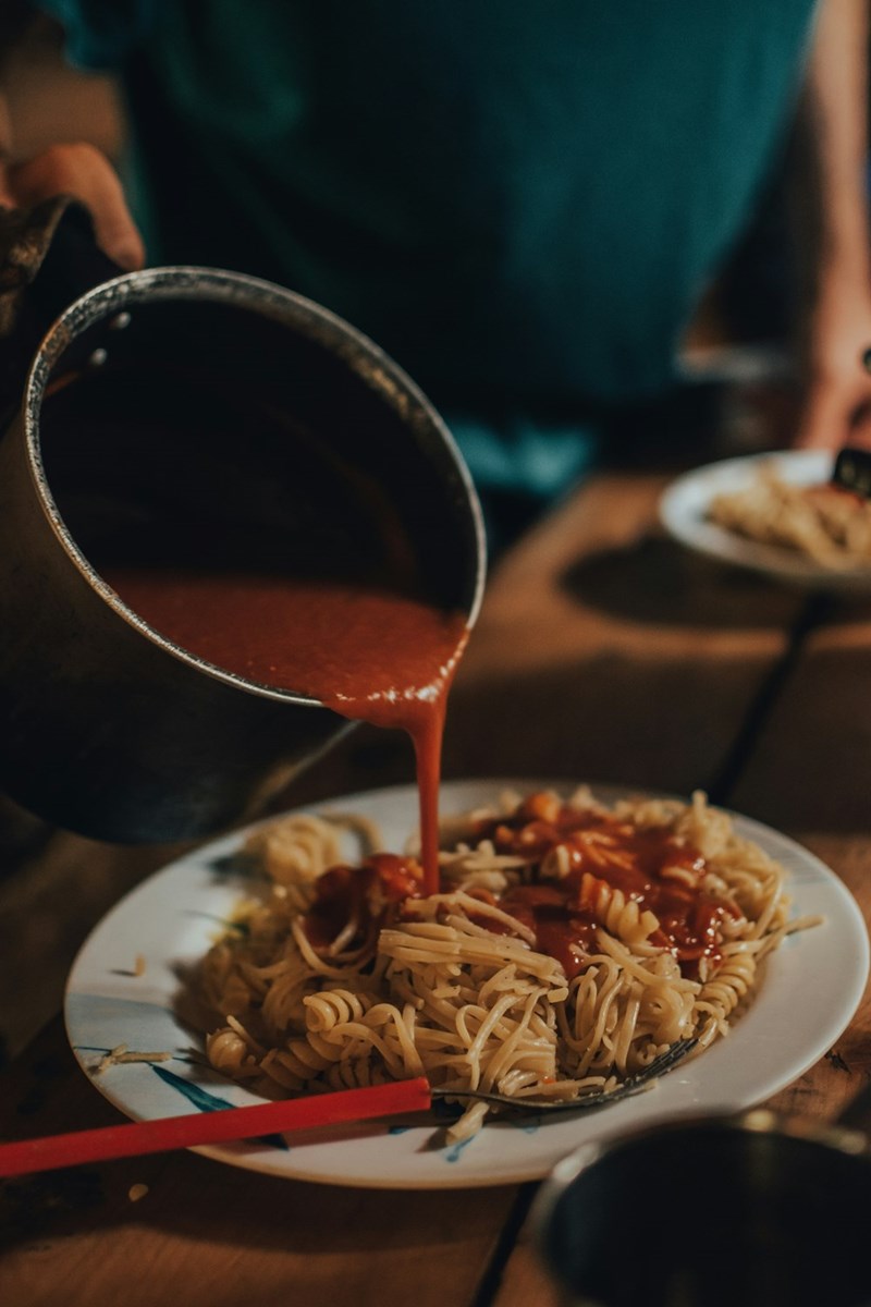 A plate of pasta served with cheese and tomato sauce being poured over it