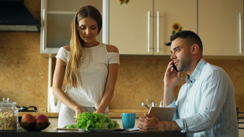 Girlfriend cooks while boyfriend talks with someone over the phone