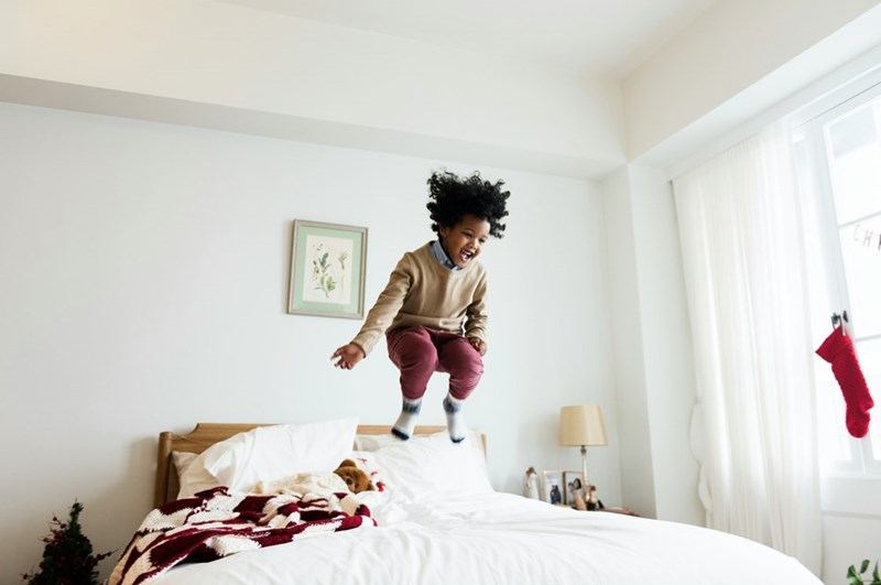 A young child jumps up and down on a bed