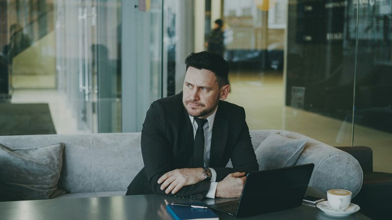 Man in a suit sitting at a table with laptop and coffee